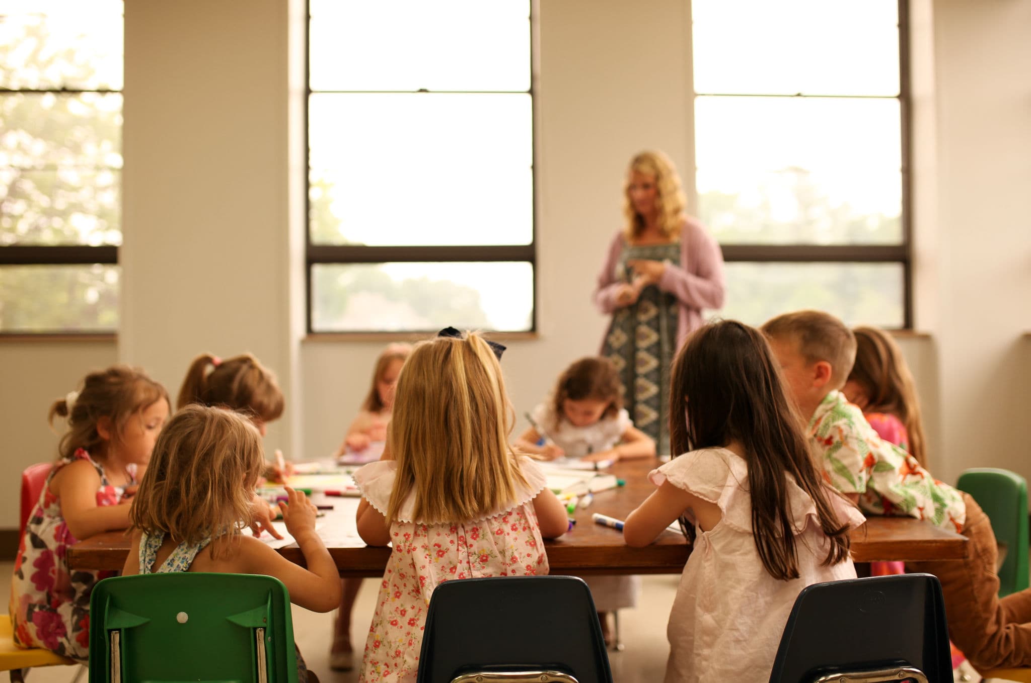 Children attentively engaged in activities at a table during a Sunday school class, with a teacher guiding them in the background.